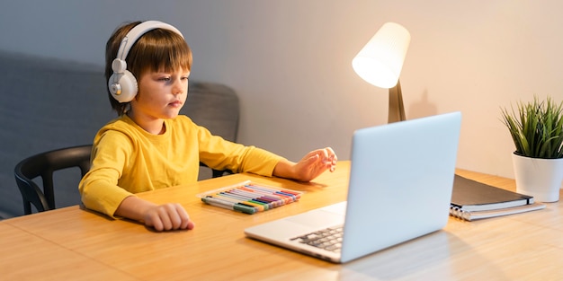 Side view school boy in yellow shirt taking virtual classes