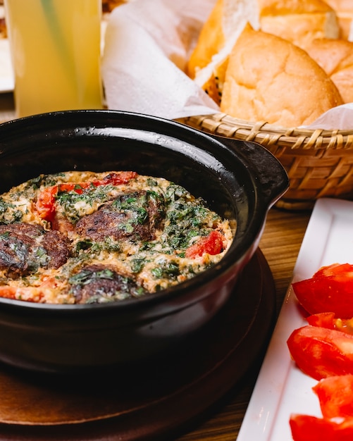 Вид сбоку яичница-болтунья с фрикадельками и зеленью в нарезанной сковороде ‹помидор и хлеб
