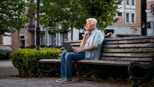 ノートパソコンとベンチに屋外の年配の男性人の側面図