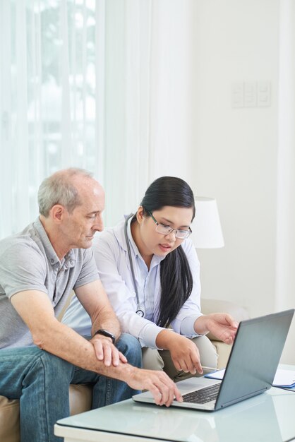 Side view of senior patient browsing the net on laptop with doctor