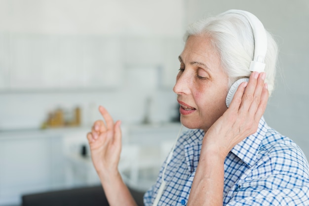 Side view of senior woman listening music on headphone singing