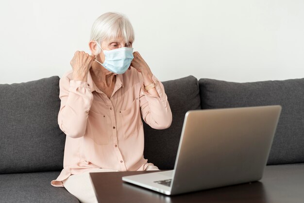 Side view of senior woman with laptop putting on medical mask