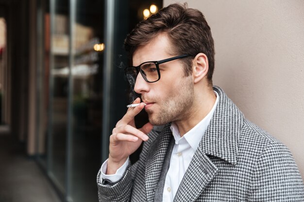 Вид сбоку серьезного бизнесмена в очки и пальто