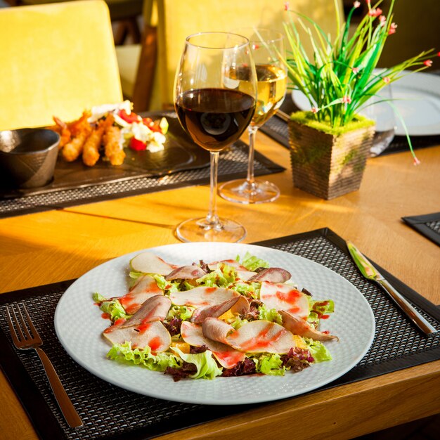 Side view served table shrimp in batter with lettuce, tomatoes and sauce on a black plate, plate with salad, glasses of wine