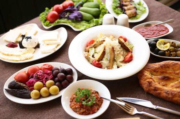 Вид сбоку на сервированный стол с различными блюдами, салат Цезарь, маринованные овощи, сырная тарелка и свежие овощи
