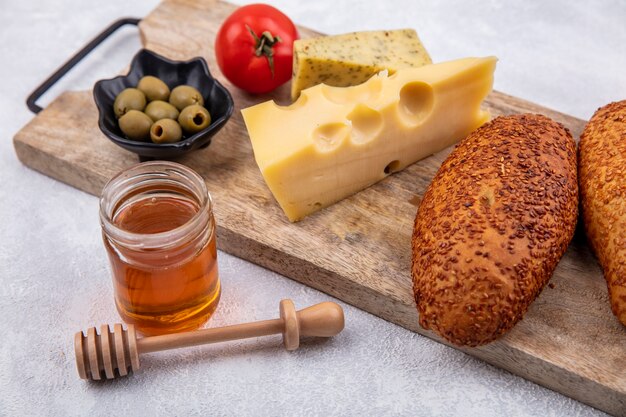 Side view of sesame patties on a wooden kitchen board with green olives on a black bowl and cheese with honey on a white background