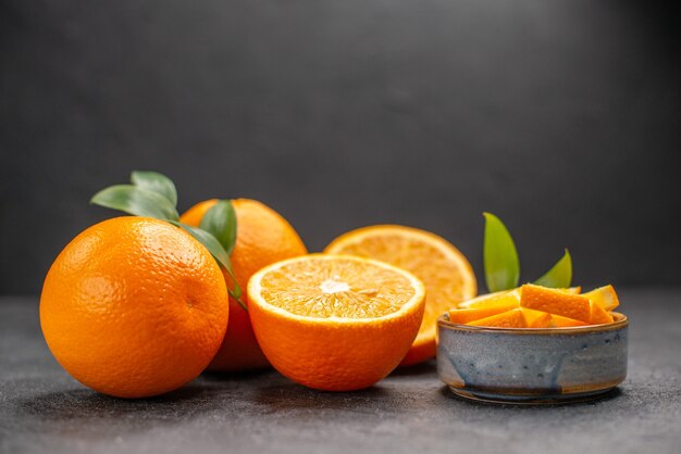 Side view of set of yellow whole and chopped oranges on dark table