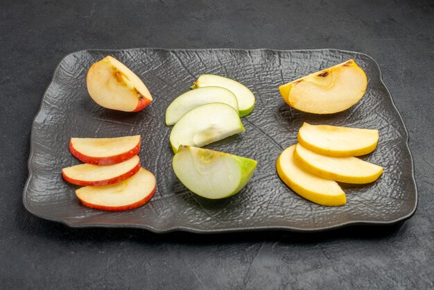 Side view of several types of sliced fresh apples on a black tray on a dark background