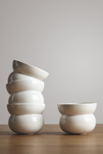 Бесплатное фото Вид сбоку в форме пустых белых простых керамических кофейных чашек в пирамиде на толстом деревянном столе изолированы
