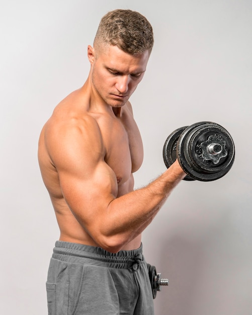 Side view of shirtless fit man posing while holding weights