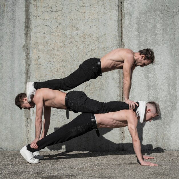 Side view of shirtless hip hop performers posing on top of each other