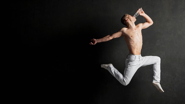 Side view of shirtless male dancer posing in mid-air with copy space