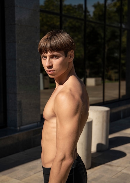 Side view of shirtless man posing outdoors while working out