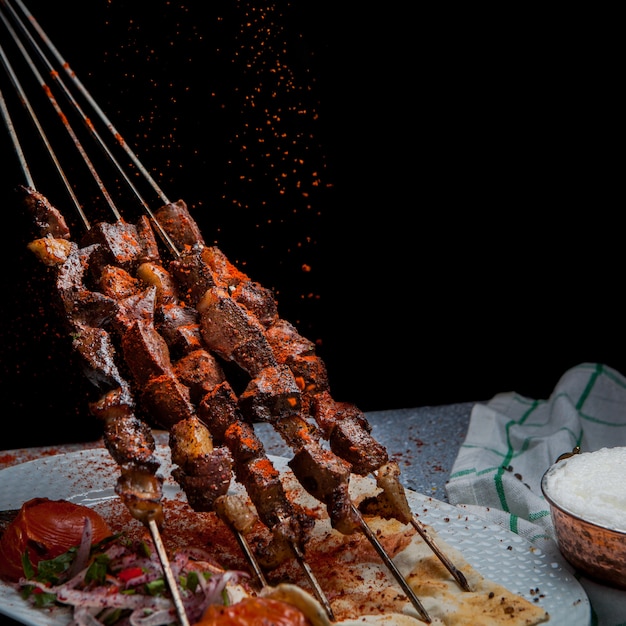 Side view shish kebab on skewers with tomato and paper and ayran in white plate