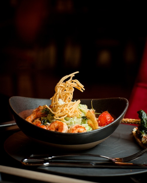 Side view of shrimp caesar plate topped with potato shoestrings