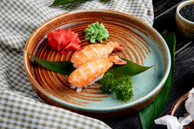 Side view of shrimp nigiri sushi on bamboo leaf served with pickled ginger slices and wasabi on a plate