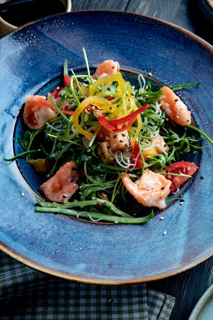 Side view of shrimp salad with bell peppers and arugula on a plate