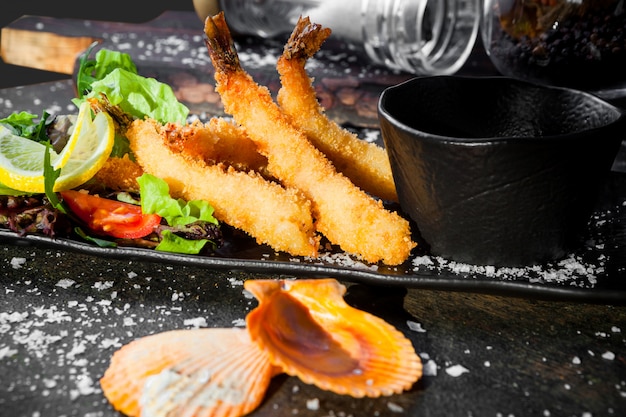 Side view shrimps in batter with bowl for sauce and fresh vegetable salad and shells in tray