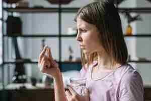 Free photo side view of a sick young woman looking at pill