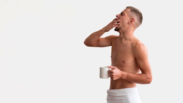 Side view of sleepy shirtless man in the morning with coffee