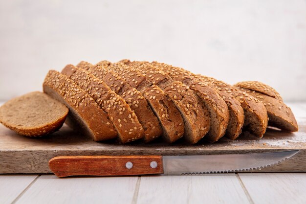 Side view of sliced brown seeded cob on cutting board and knife on wooden surface and white background