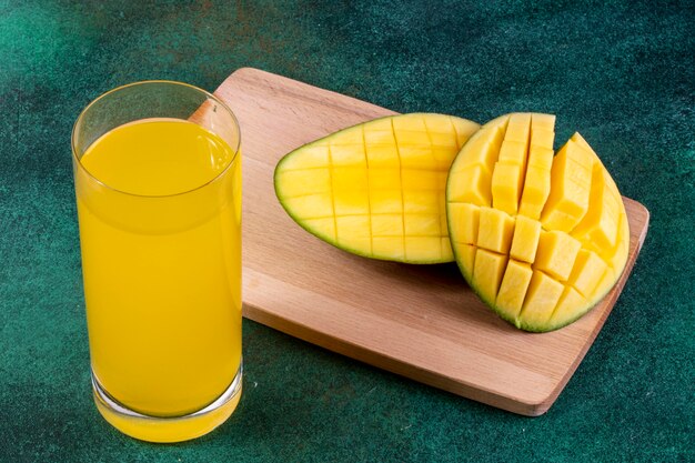 side view sliced mango on a blackboard with a glass of orange juice on a green table