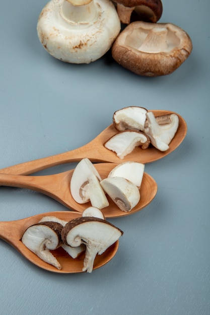 Side view of sliced mushrooms on wood spoons and whole mushrooms on light blue