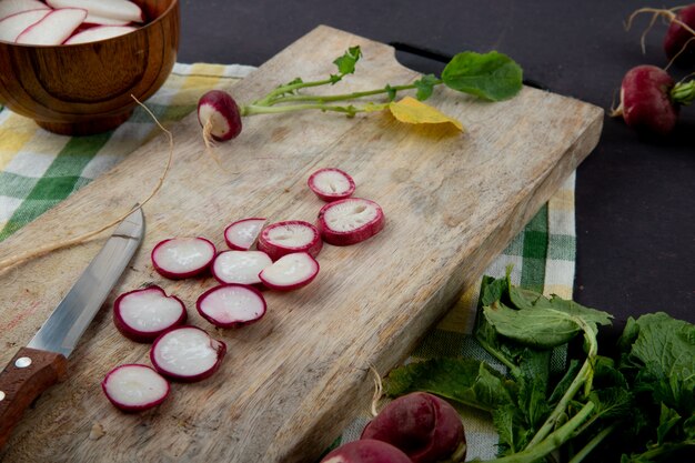 Side view of sliced red radish with knife on wooden surface on cloth and maroon background