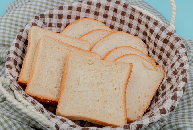 side view of sliced white bread in basket on plaid cloth and blue