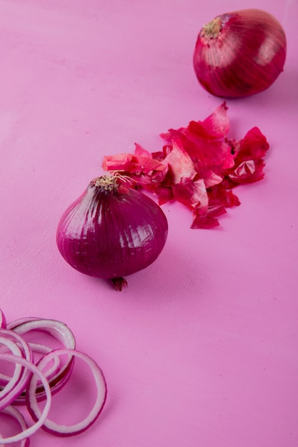 Side view of sliced and whole onion with skin on purple background with copy space