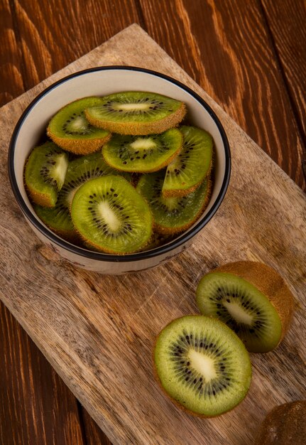 Side view of slices of kiwi fruit in a bowl on wood board on rustic