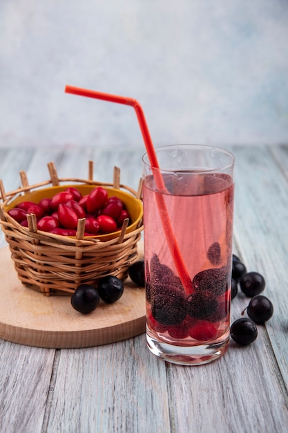 Side view of small sour red cornel berries on a bucket on a wooden kitchen board with cornel berry juice and blackthorn on a grey wooden background