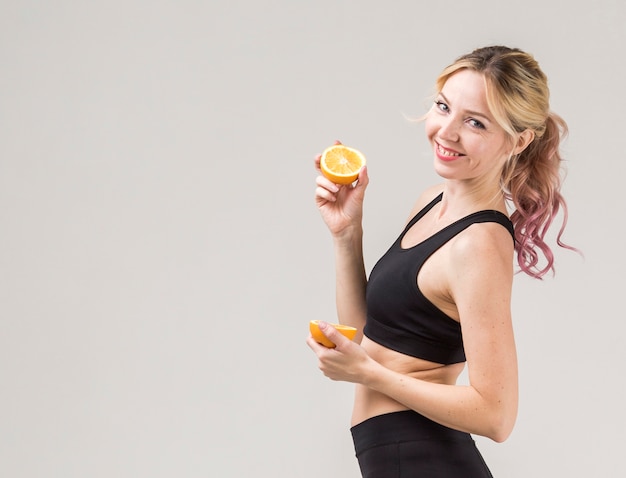 Side view of smiley athletic woman posing with oranges