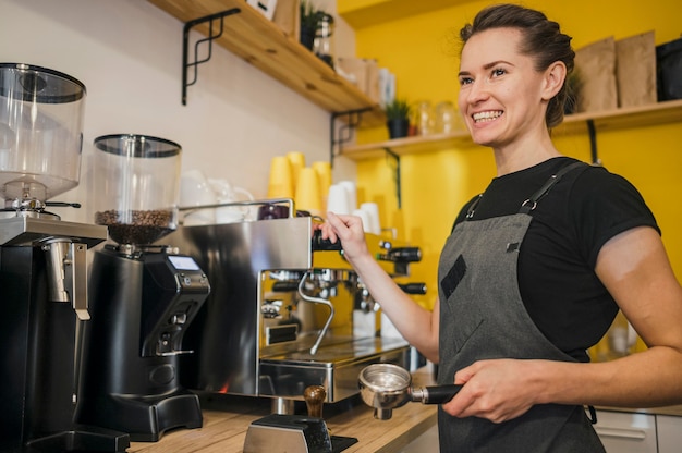 Free photo side view of smiley barista using coffee machine