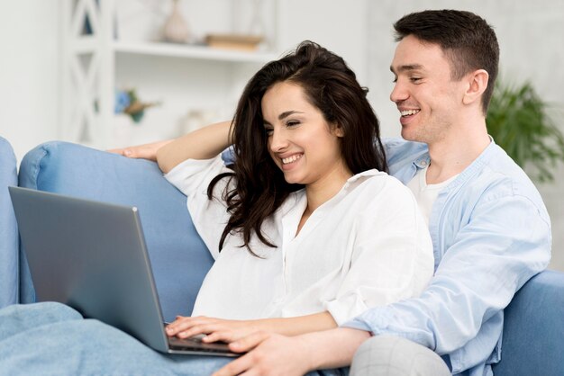 ソファーでノートパソコンを見て笑顔のカップルの側面図
