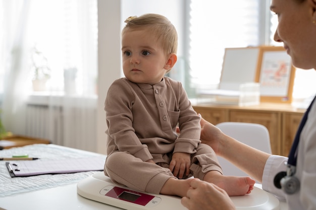 Free photo side view smiley doctor weighing baby