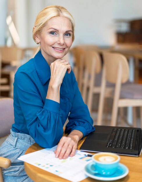 ノートパソコンでの作業とコーヒーを飲みながらポーズスマイリー長老ビジネス女性の側面図