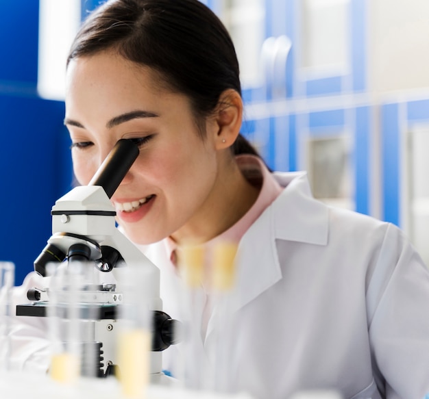 Free photo side view of smiley female scientist in the lab using microscope