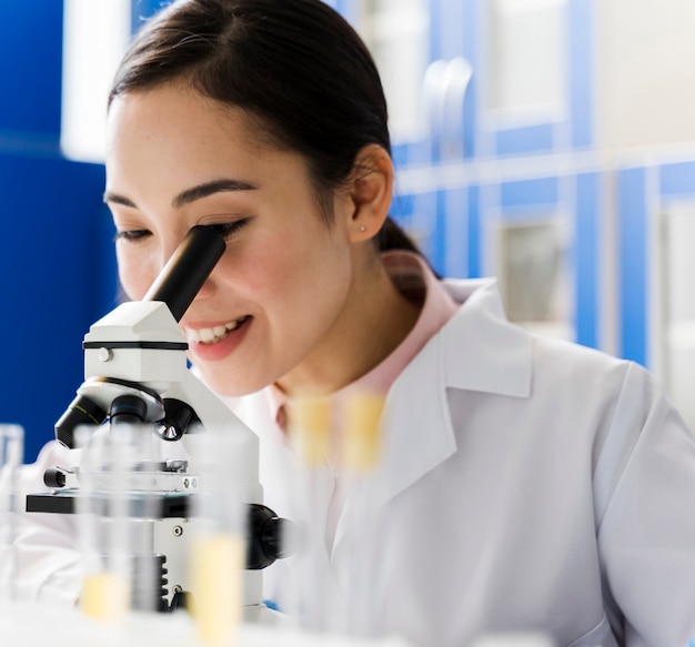 Foto gratuita vista laterale della scienziata sorridente in laboratorio usando il microscopio