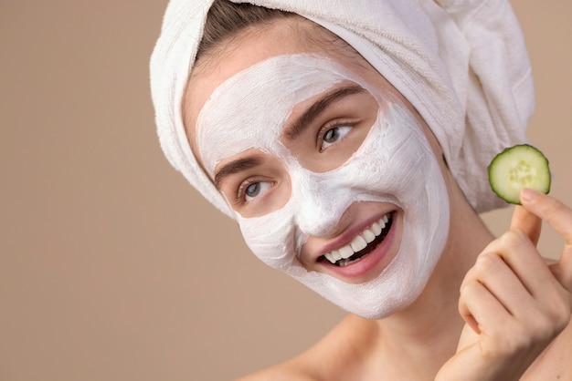 Foto gratuita ragazza sorridente di vista laterale con maschera facciale e cetriolo