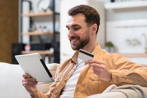 Side view of smiley man holding tablet and credit card