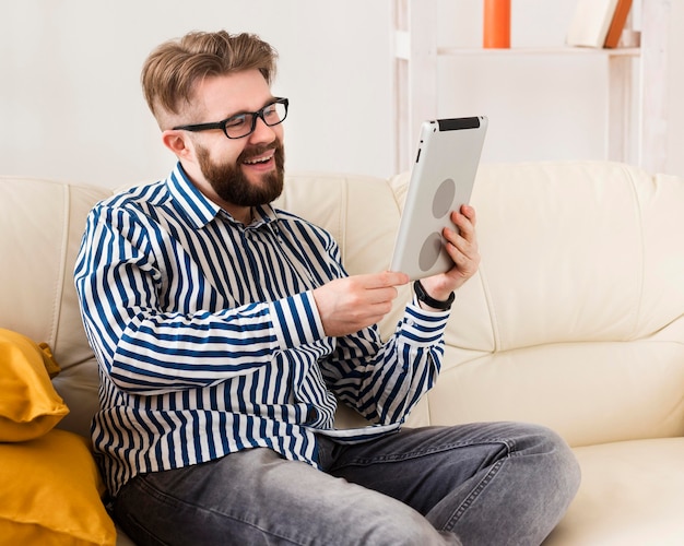 Side view of smiley man on sofa with tablet