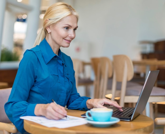 Side view of smiley older business woman working on laptop with papers