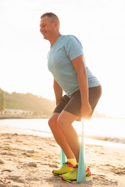 Side view of smiley senior man working out with elastic rope on the beach