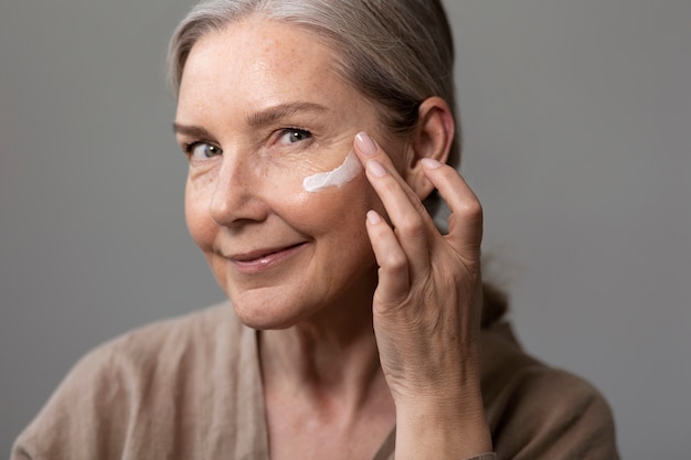 Foto gratuita donna sorridente di vista laterale che applica crema per il viso