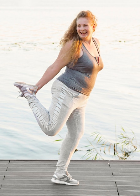 Free photo side view of smiley woman by the lake stretching