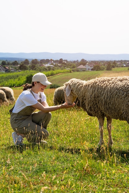Вид сбоку улыбающаяся женщина кормит овец