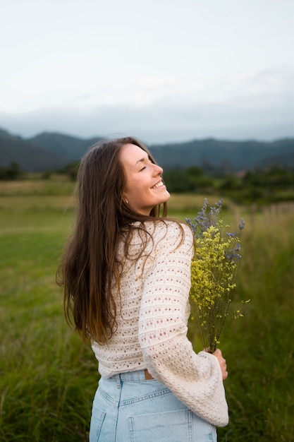 무료 사진 꽃을 들고 측면 보기 웃는 여자