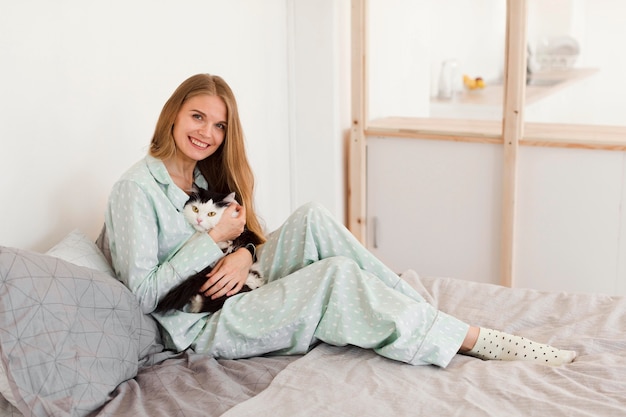 Side view of smiley woman in pajamas on bed holding cat