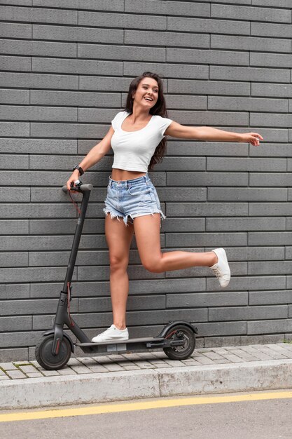 Side view of smiley woman posing with scooter outside